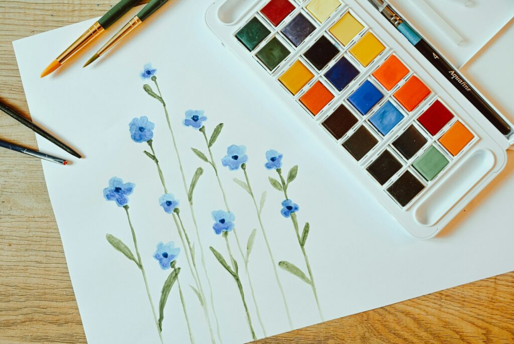 Watercolor paints and a floral painting on paper.